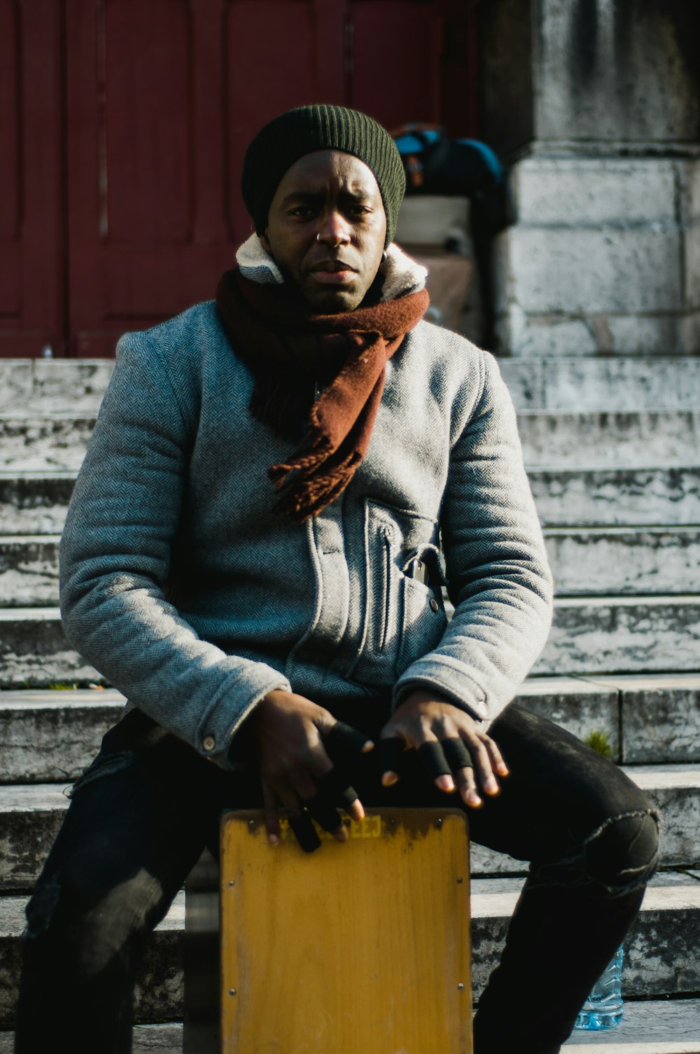 man sitting on brown cajon near gray stairs