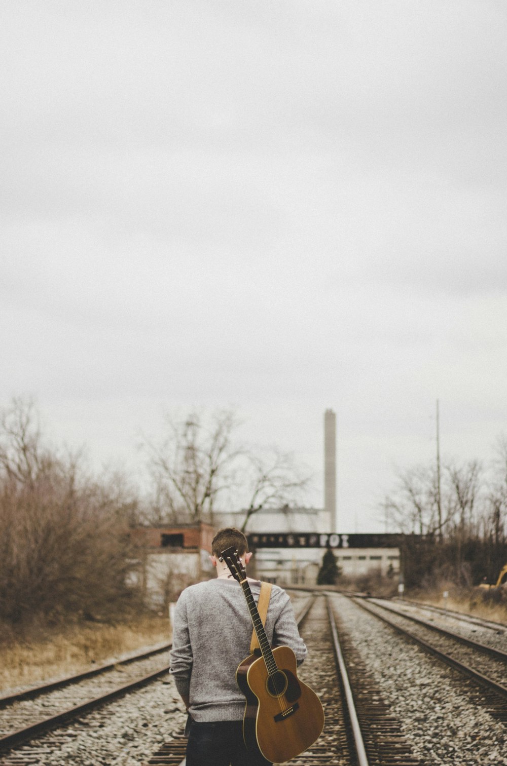 Mann mit Gitarre geht auf Zugschienen
