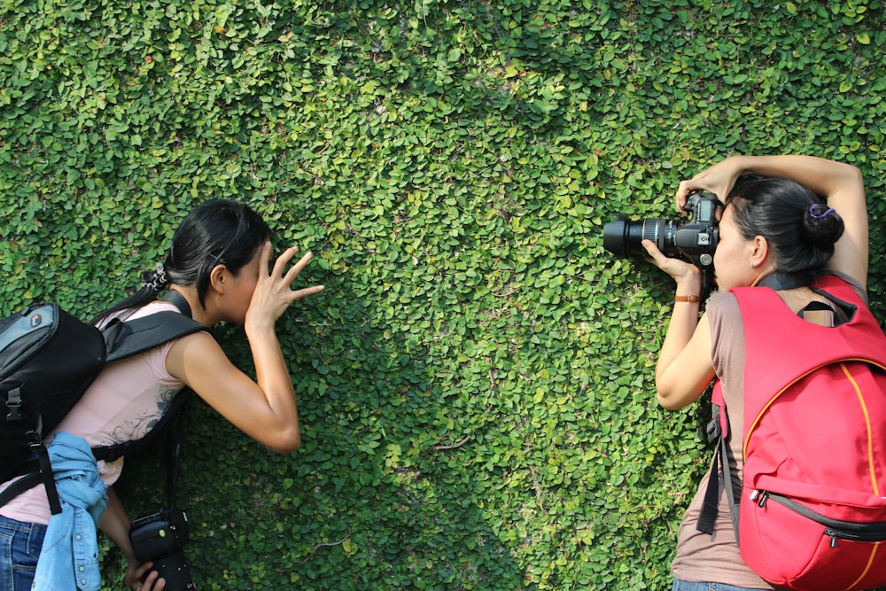 woman taking a picture of woman leaning in a green grass wall
