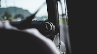Inside view of a vehicle focusing on the air ventilation system, with a blurred background showing a road and distant hills. The scene is captured from the passenger side, emphasizing the car's interior elements and the view outside is slightly out of focus.
