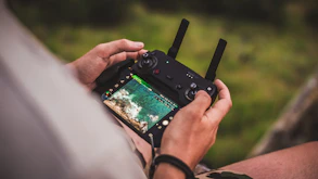 A close-up shot of a drone pilot controlling the FPV drone with a remote in an open field.