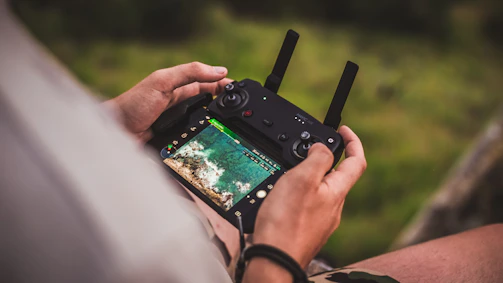 Close-up of hands adjusting a drone controller as it hovers over a scenic coastline.