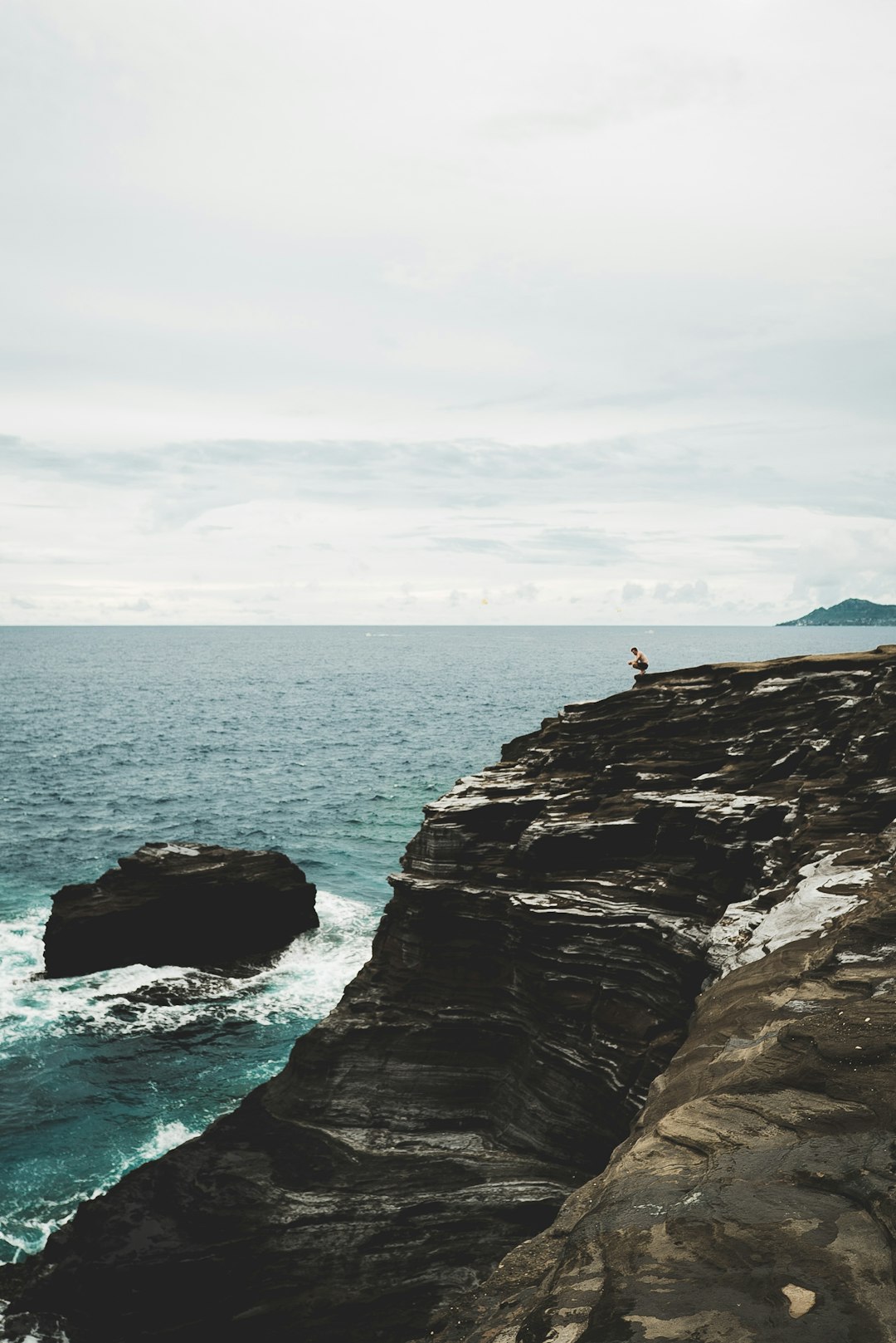 person sitting on cliff near body of water