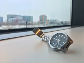 Side profile of a modern stainless steel watch glistening against a monochrome cityscape backdrop.