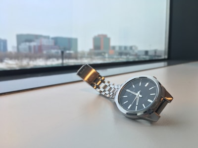 A sleek watch with clean lines resting on a concrete ledge overlooking a London skyline at dusk.