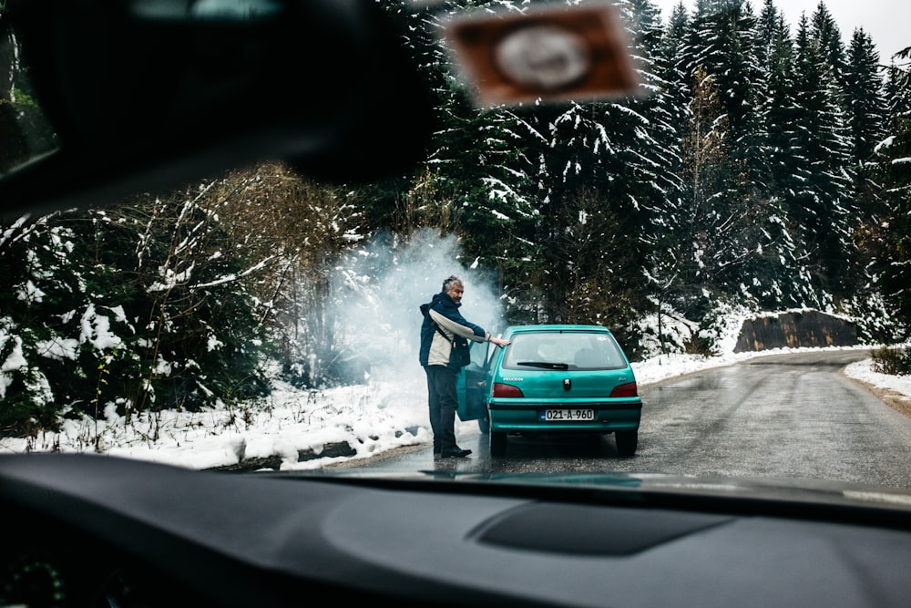 Hombre de pie frente a un vehículo verde azulado hatchback