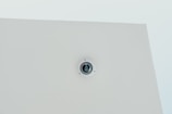 A security camera is mounted on a flat white ceiling, centrally positioned, with a minimalist and clean appearance.