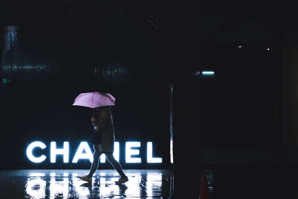 mujer que camina bajo el paraguas pasando por la señalización iluminada de Chanel