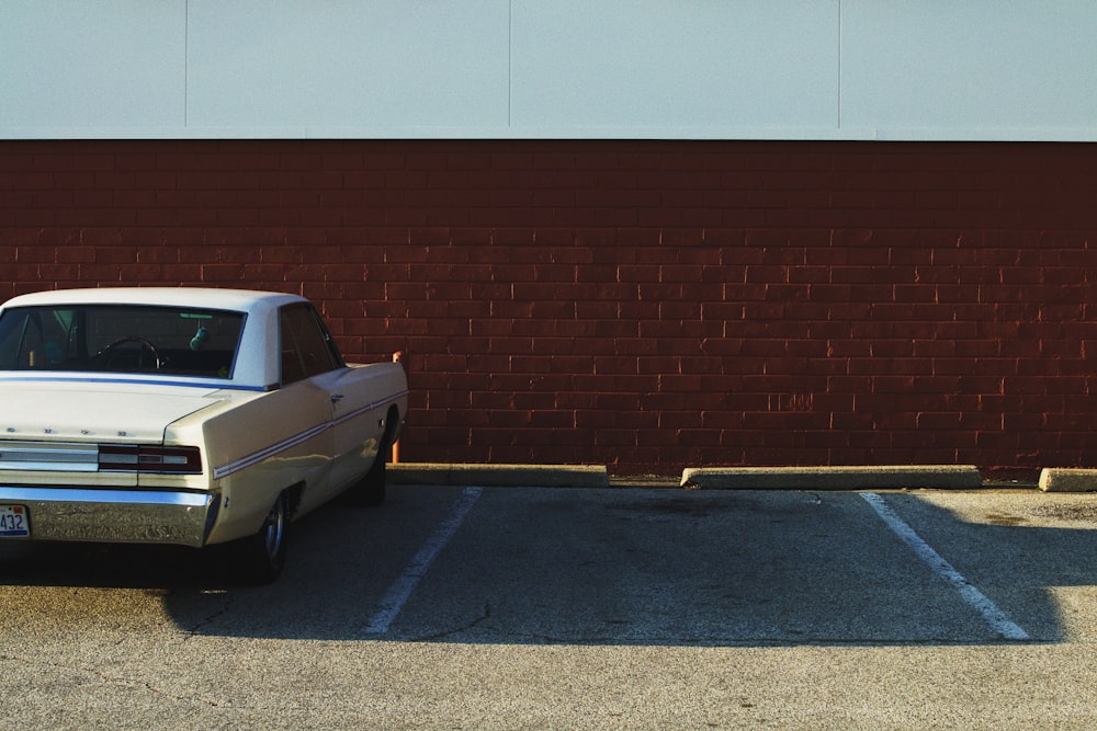 Voiture blanche garée sur le parking près d’un mur brun et blanc