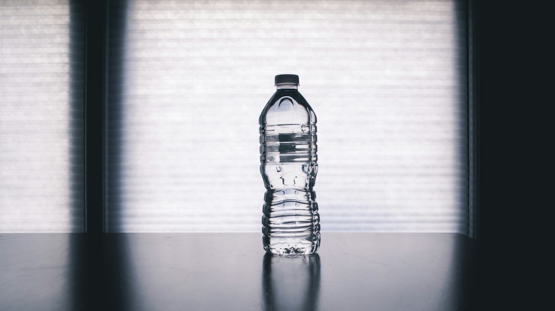 Person drinking water from a bottle outdoors on a hot sunny day