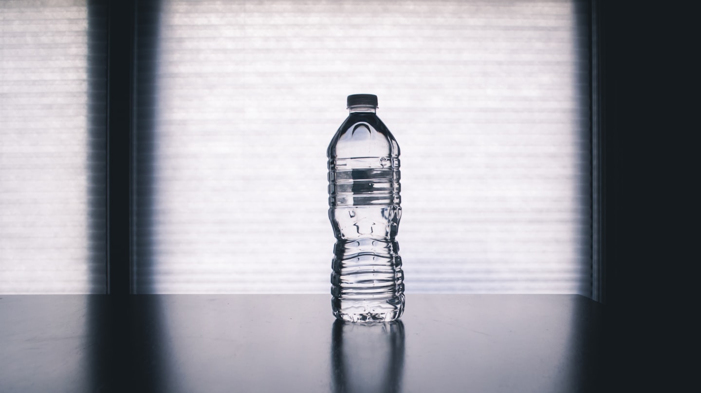 A clear water bottle on a dark table lit by soft daylight