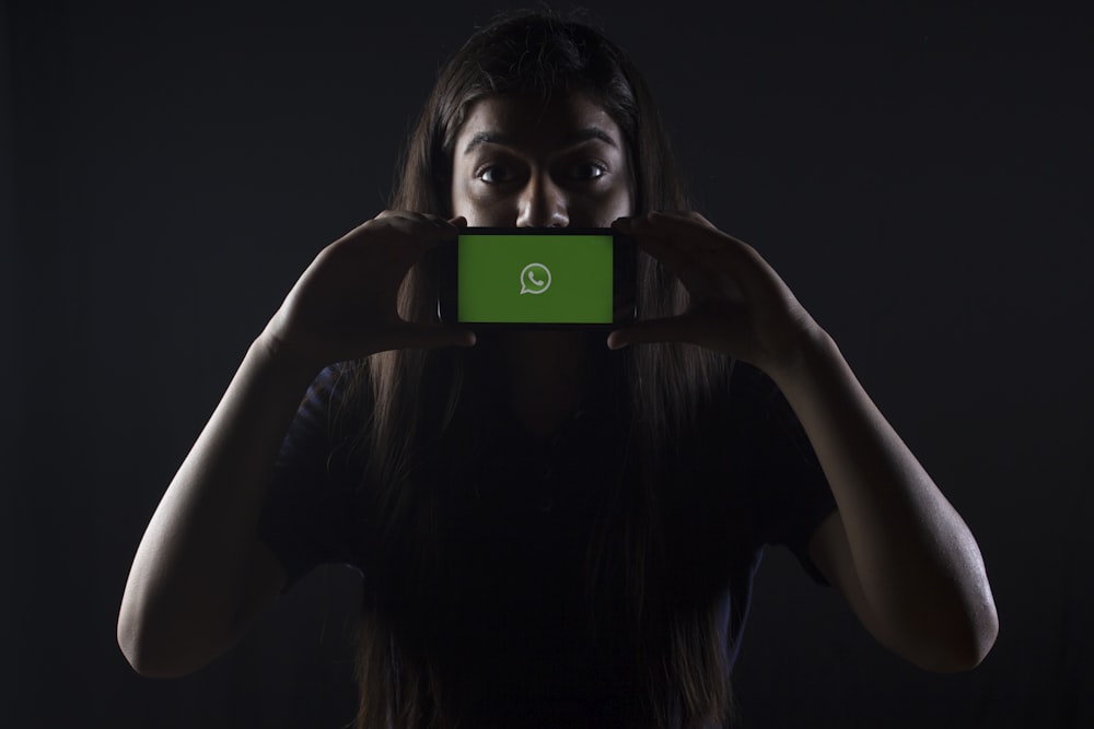 Frau hält schwarzes Smartphone am Whatsapp-Logo