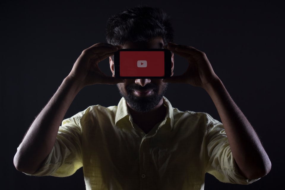 A man holding a phone displaying the YouTube logo in front of his face.