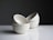 Four white ceramic bowls are neatly stacked in an asymmetrical arrangement on a glossy white surface. The background is a smooth, dark gradient, creating a contrast with the simplicity and elegance of the bowls.