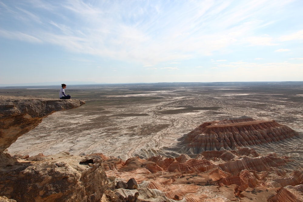 photography of person sitting on mountain cliff at daytime
