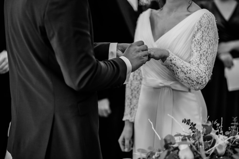 Foto em tons de cinza do homem inserir anel na mulher durante a cerimônia de casamento
