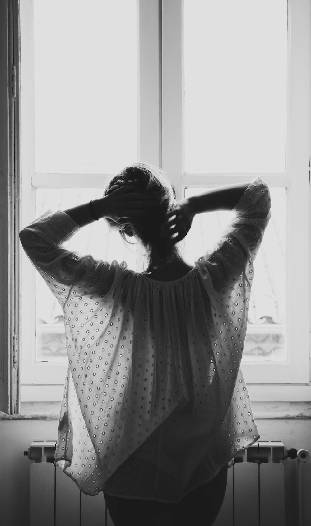 grayscale photograph of woman standing in front of window