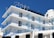 A multi-story hotel building with a clear blue sky backdrop. The structure features several balconies with blue railings and glass panels. The exterior is predominantly white, and the top displays an antenna and satellite dish. The word 'HOTEL' is prominently displayed at the rooftop section.