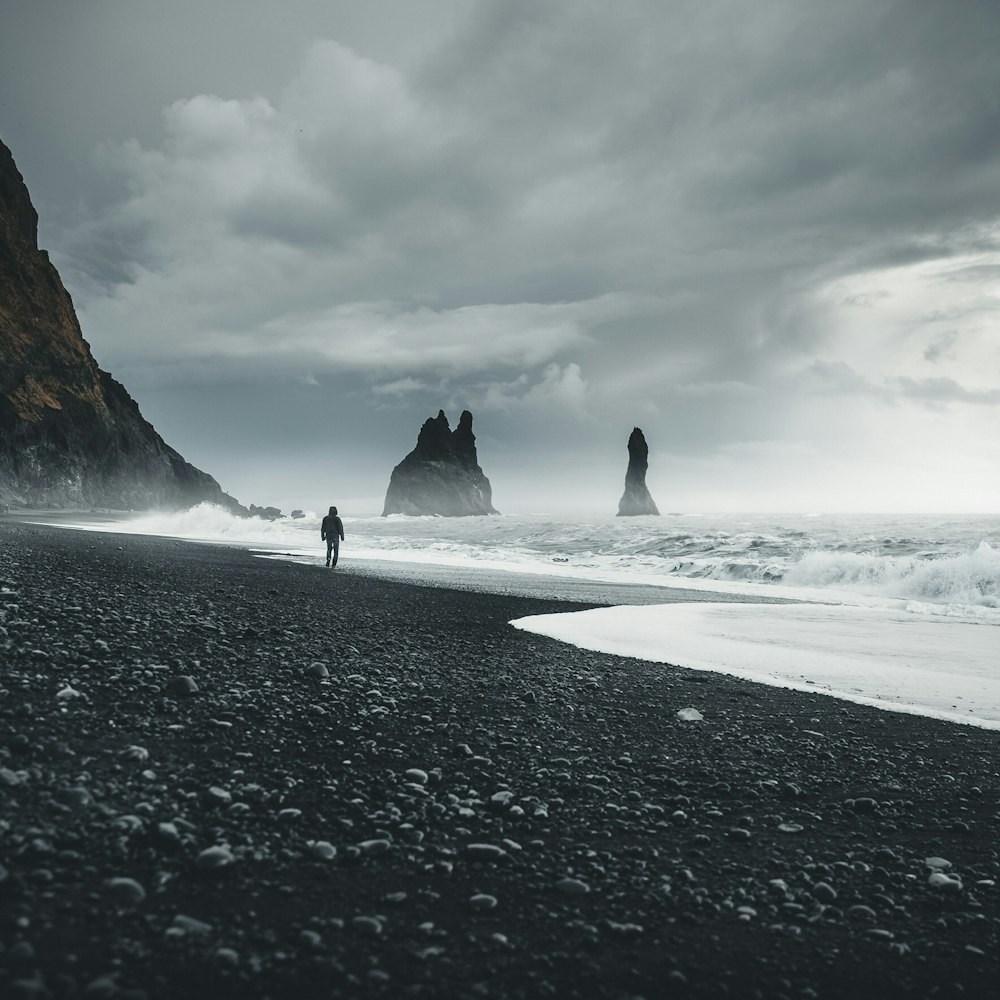 person standing on shore near rock formation at daytime