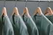 A row of green t-shirts hanging on wooden hangers, each evenly spaced along a metallic clothing rack.