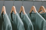 A row of green t-shirts hanging on wooden hangers, each evenly spaced along a metallic clothing rack.