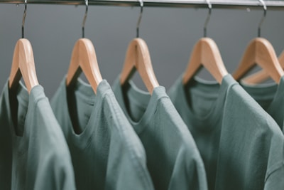 A row of green t-shirts hanging on wooden hangers, each evenly spaced along a metallic clothing rack.