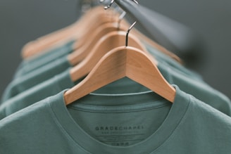 A collection of green shirts neatly hung on wooden hangers, aligned in a row with a focus on the closest garment. The soft lighting creates a calm and organized atmosphere.