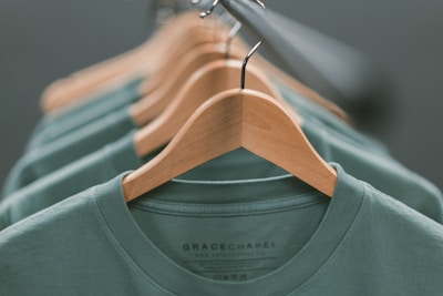 A collection of green shirts neatly hung on wooden hangers, aligned in a row with a focus on the closest garment. The soft lighting creates a calm and organized atmosphere.