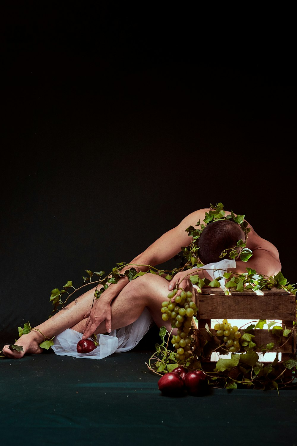 person laying down against brown box with grapes covering him
