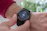 A close-up view of a person's wrist wearing a black smartwatch with a touchscreen displaying fitness statistics such as steps, calories burned, and distance. The person is wearing a red sweater and is interacting with the watch using their other hand.