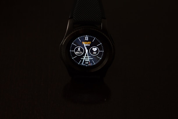A smartwatch with a round dial is prominently displayed against a dark background. The digital screen shows various information such as time, date, heart rate, and steps. The watch face is illuminated, featuring a design with numbers, while icons indicating activity and heart monitoring are visible.