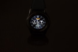 A smartwatch with a round dial is prominently displayed against a dark background. The digital screen shows various information such as time, date, heart rate, and steps. The watch face is illuminated, featuring a design with numbers, while icons indicating activity and heart monitoring are visible.