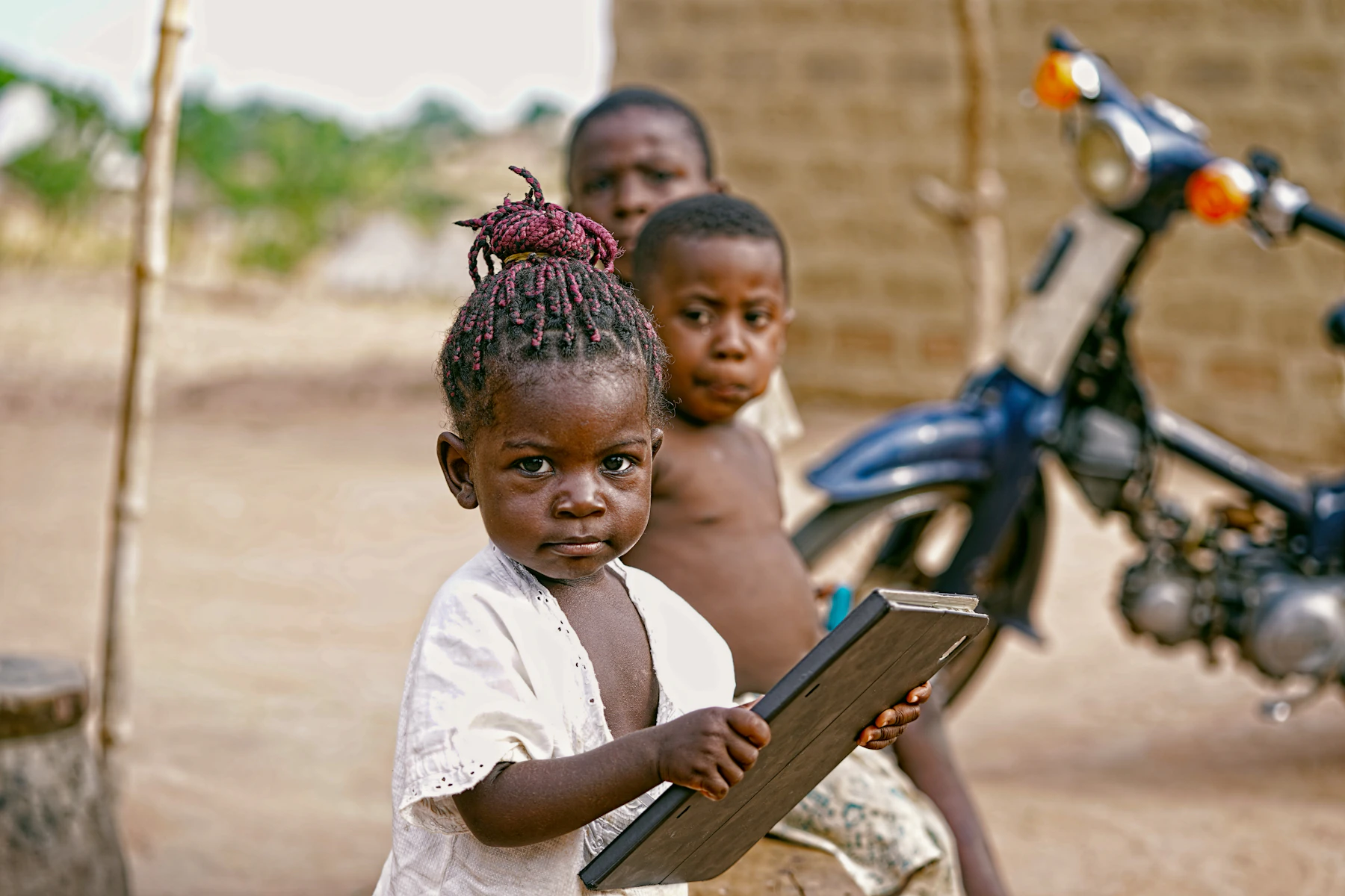 A young girl holding an open book outside with other children