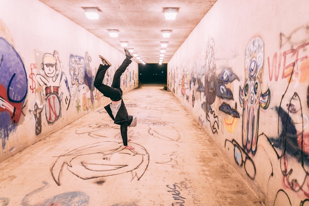 Un hombre haciendo una parada de manos en un túnel cubierto de graffiti