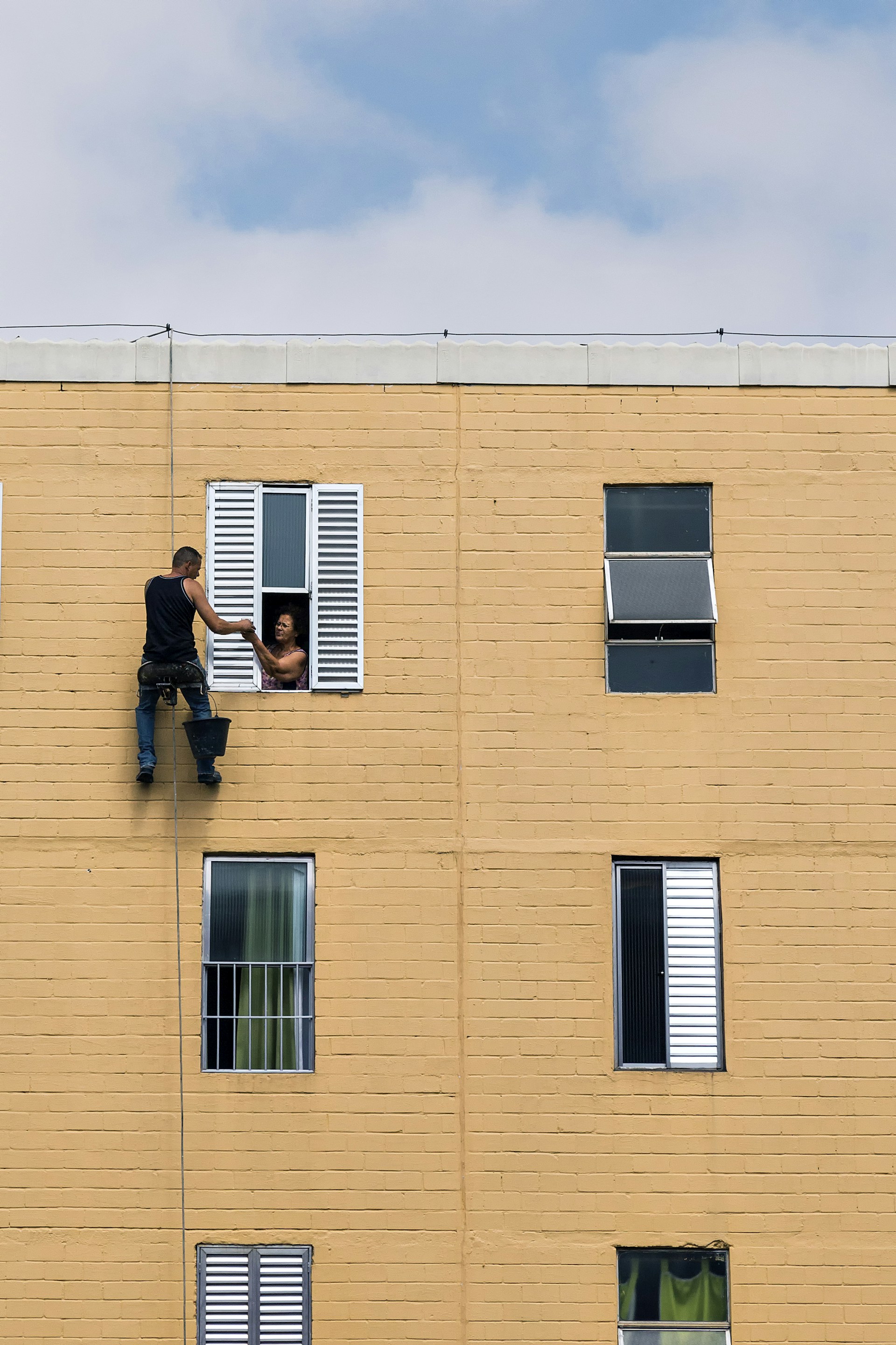 man hanging on building near woman in window during daytime