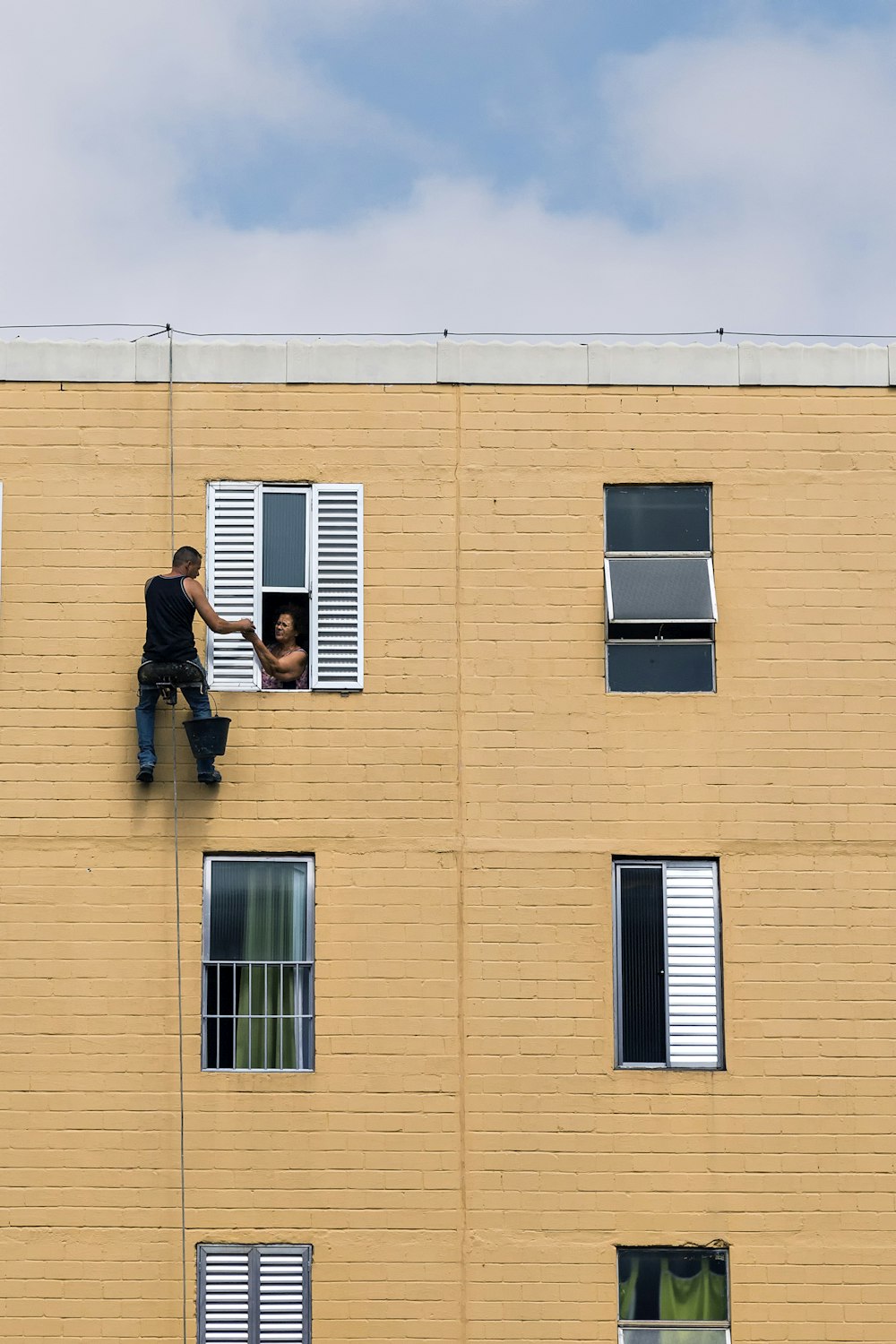 man hanging on building near woman in window during daytime