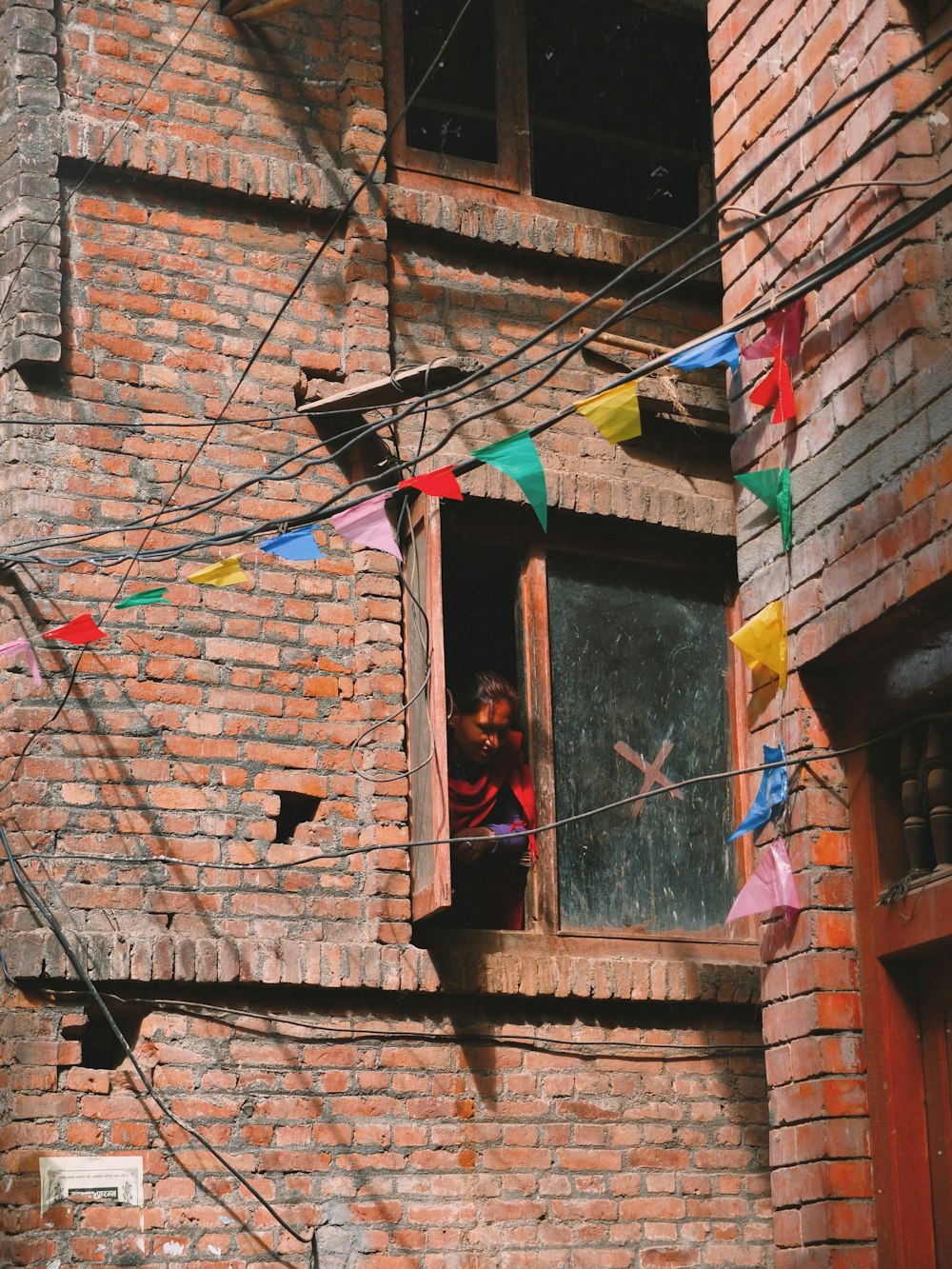 woman looking down by the window of bricked wall building
