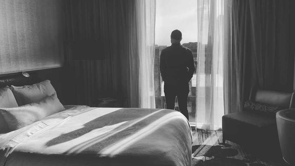 man standing in front of curtain near bed inside room