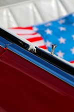 Close-up of a red car interior showing part of the door and an American flag in the background.