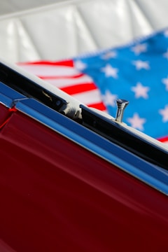 Close-up of a red car interior showing part of the door and an American flag in the background.