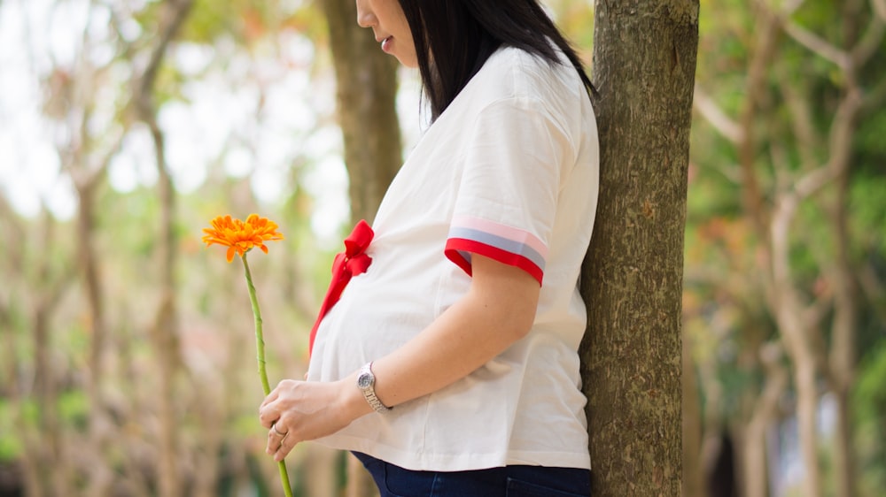 Mulher segurando a flor de laranja apoiando-se na árvore