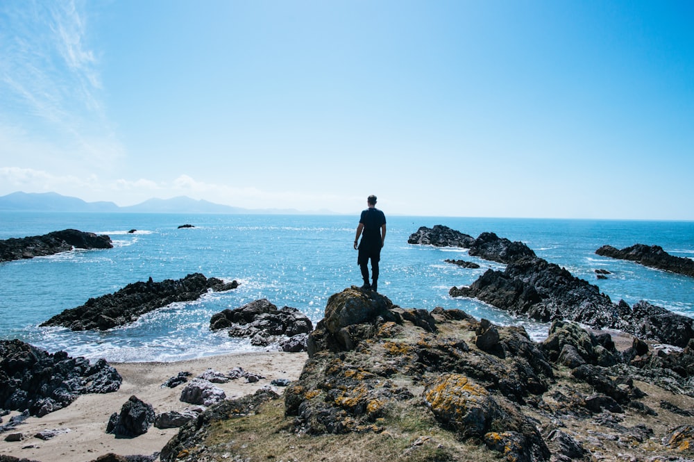 man standing on top of rock formation near body of water