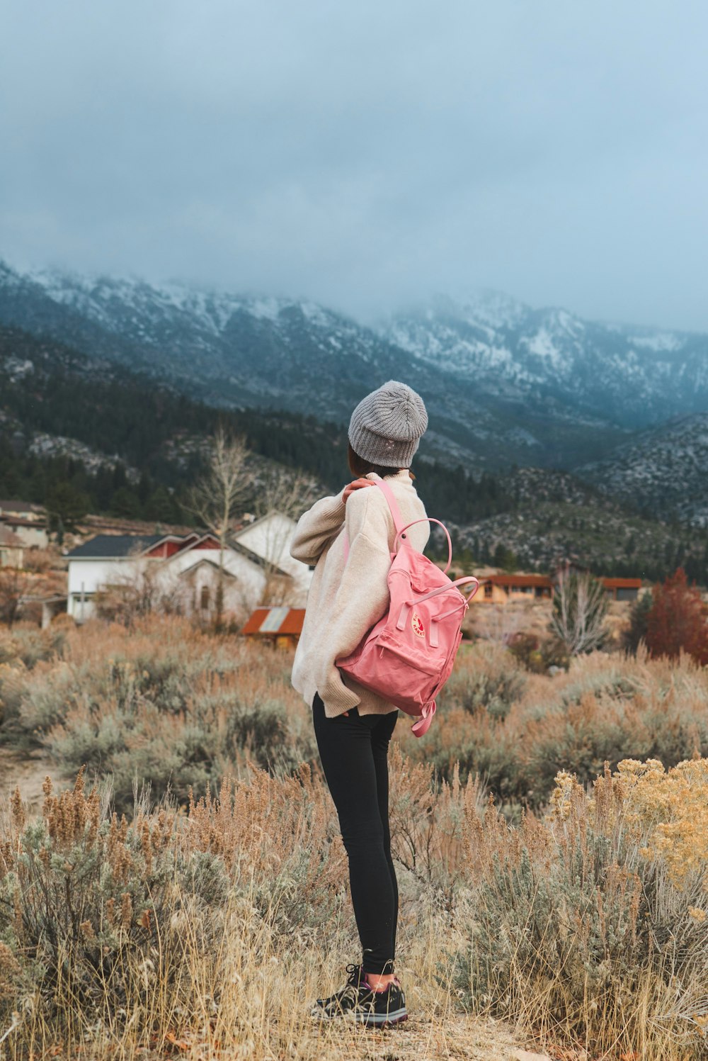 Frau mit rosa Rucksack steht in der Nähe von Gras mit Blick auf die Berge