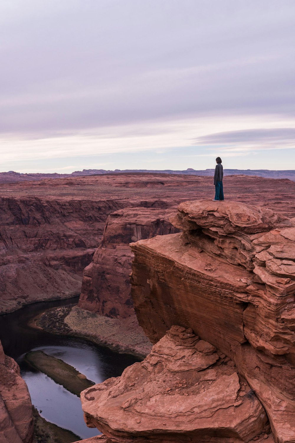 woman standing on cliff under cloudy sky