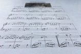 A close-up view of a sheet of music displaying various musical notes and symbols, written in a traditional style on a plain background. The focus is on the arrangement of notes and the linear staff, conveying a sense of musical composition.