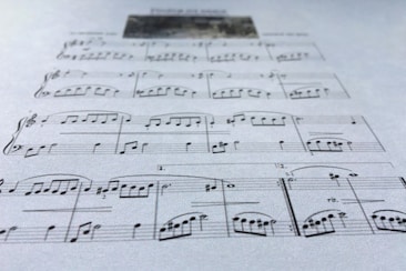 A close-up view of a sheet of music displaying various musical notes and symbols, written in a traditional style on a plain background. The focus is on the arrangement of notes and the linear staff, conveying a sense of musical composition.