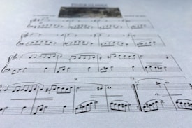 A close-up view of a sheet of music displaying various musical notes and symbols, written in a traditional style on a plain background. The focus is on the arrangement of notes and the linear staff, conveying a sense of musical composition.