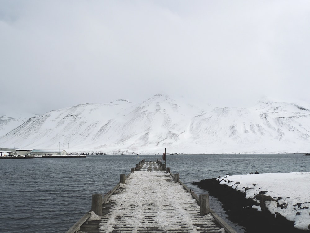 wooden pier on river near snowy mountains