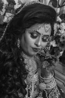 Side view of a bride smiling while her mehndi is being applied, surrounded by rich green and gold decor.
