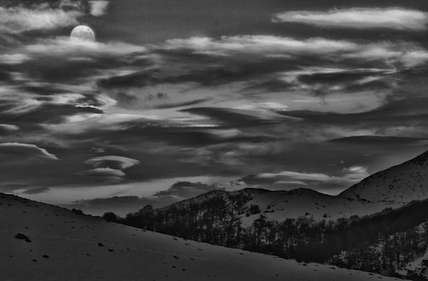Dramatic black and white landscape with mountains under a full moon.